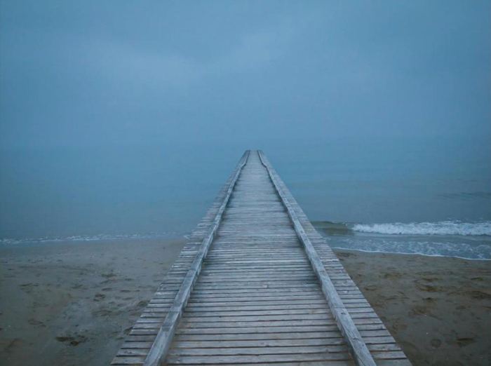 A wooden boardwalk leading into a misty blue sea