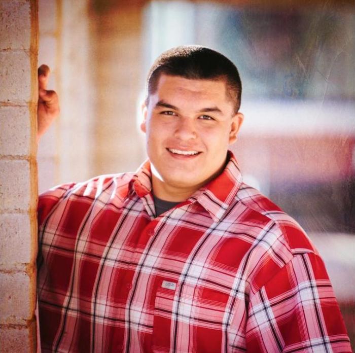 Smiling young man in a red plaid shirt leaning on a brick wall