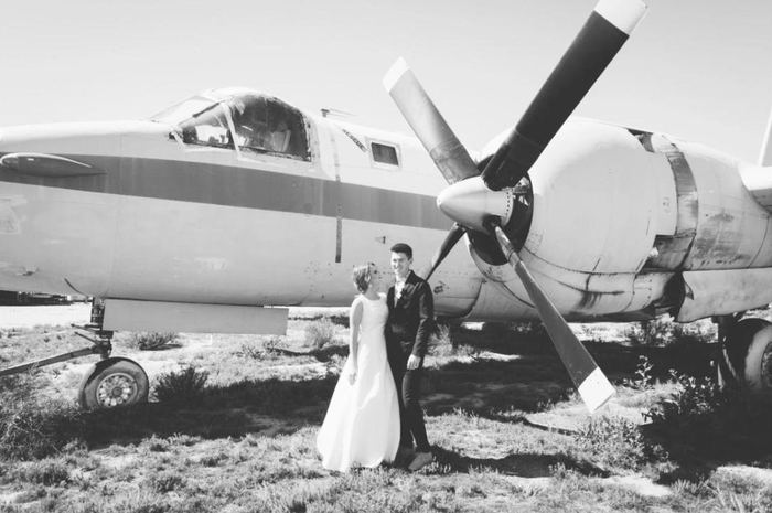 Newlyweds beside a vintage propeller plane, black and white