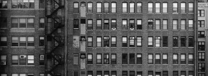 Black and white facade of a brick apartment building with fire escapes