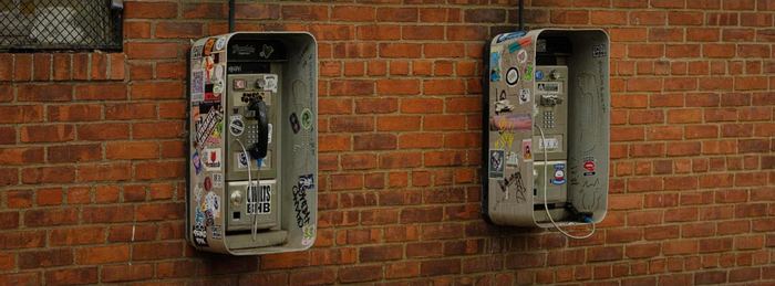 Two sticker-covered payphones on a brick wall