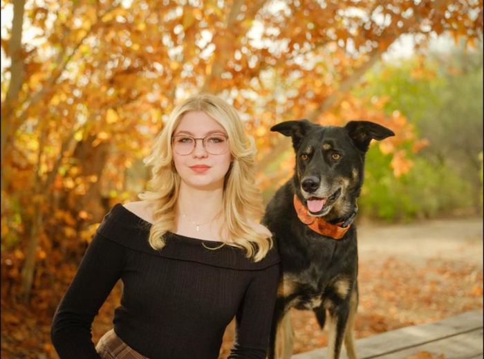 Young woman and her dog in front of golden autumn trees