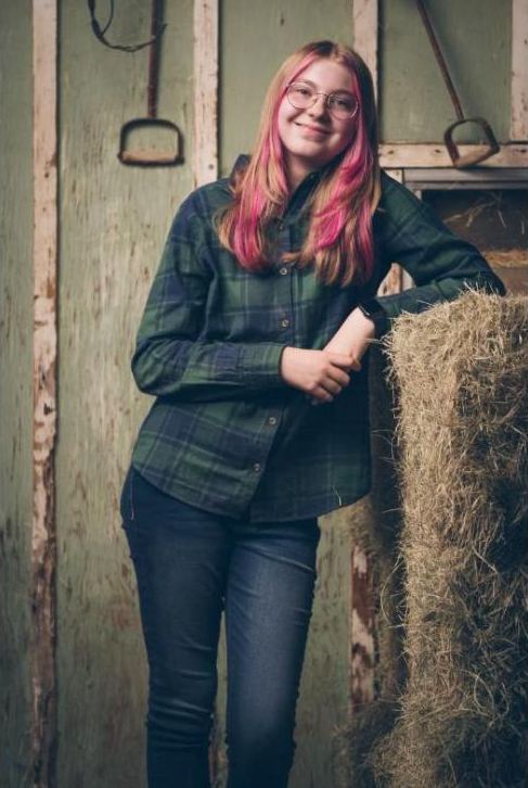 Portrait of a young woman leaning on a hay bale in a barn